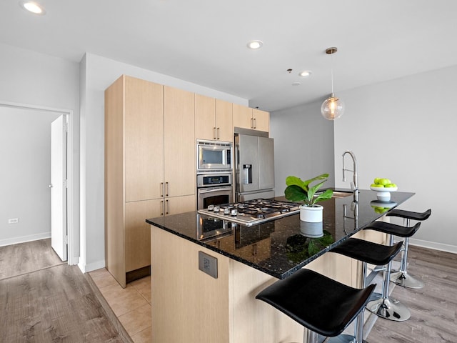 653 N Kingsbury St Unit 1707, Chicago, IL 60654 - kitchen with appliances with stainless steel finishes, light brown cabinetry, a kitchen breakfast bar, dark stone counters, and recessed lighting