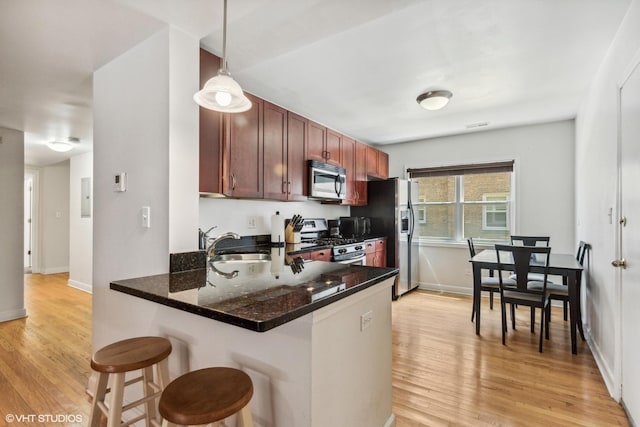 6427 N Damen Ave Unit 1E, Chicago, IL 60645 - kitchen with appliances with stainless steel finishes, a kitchen breakfast bar, light wood-style floors, a peninsula, and decorative light fixtures