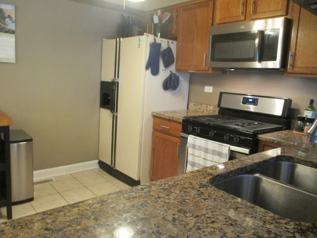 865 N Tamarac Blvd, Addison, IL 60101 - kitchen featuring appliances with stainless steel finishes, brown cabinets, light tile patterned flooring, and dark stone countertops