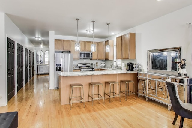 1900 N Laramie Ave, Chicago, IL 60639 - kitchen featuring appliances with stainless steel finishes, a peninsula, light wood-style flooring, hanging light fixtures, and light stone countertops