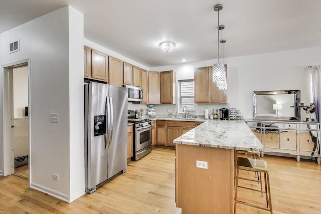 1900 N Laramie Ave, Chicago, IL 60639 - kitchen with stainless steel appliances, a peninsula, light wood-style floors, a kitchen bar, and decorative light fixtures