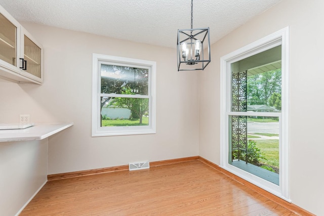 741 Gates St, West Chicago, IL 60185 - unfurnished dining area featuring light wood-style flooring, a chandelier, and a textured ceiling