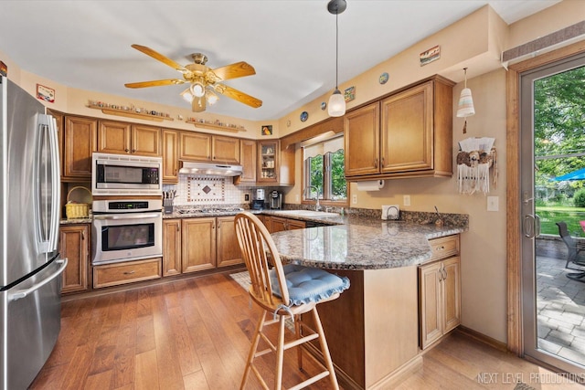 4S064 Hazelcrest Dr, Sugar Grove, IL 60554 - kitchen with stainless steel appliances, under cabinet range hood, brown cabinets, a peninsula, and hardwood / wood-style flooring