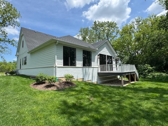 view of side of property featuring a deck, a lawn, and roof with shingles