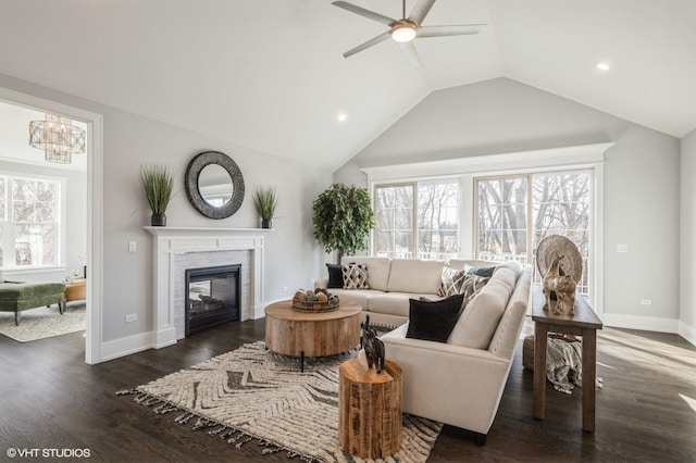 living area featuring a ceiling fan, a glass covered fireplace, plenty of natural light, lofted ceiling, and dark wood-type flooring