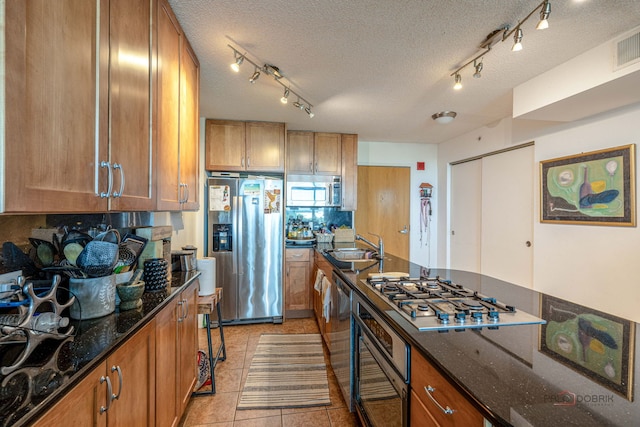 9655 Woods Dr Unit 1009, Skokie, IL 60077 - kitchen with appliances with stainless steel finishes, track lighting, a textured ceiling, dark stone countertops, and brown cabinets