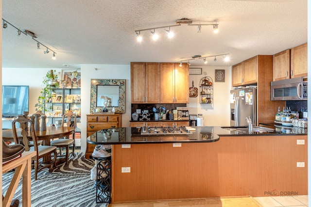 9655 Woods Dr Unit 1009, Skokie, IL 60077 - kitchen with appliances with stainless steel finishes, rail lighting, a peninsula, brown cabinetry, and a kitchen bar