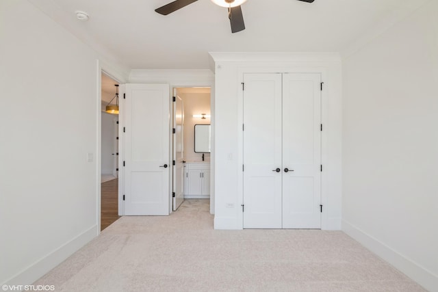 unfurnished bedroom featuring light colored carpet, ensuite bathroom, a closet, and a ceiling fan