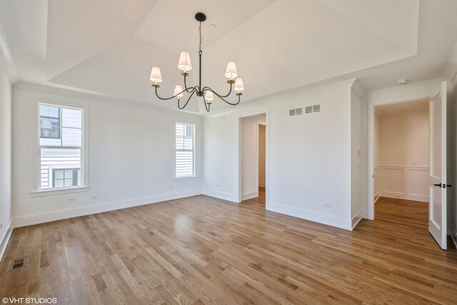 empty room featuring a chandelier, light wood-style flooring, a tray ceiling, and a smoke detector