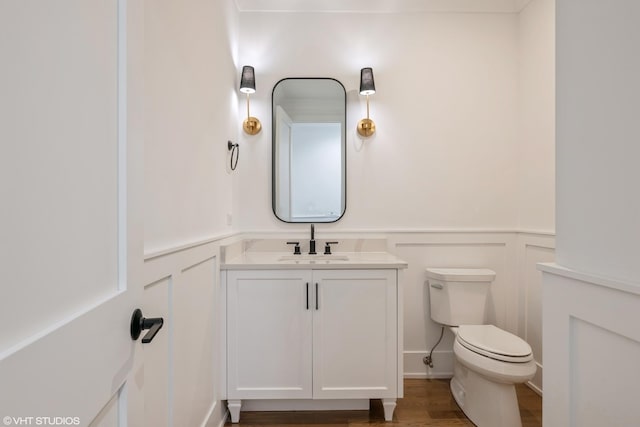 half bathroom featuring a decorative wall, vanity, wainscoting, and wood finished floors