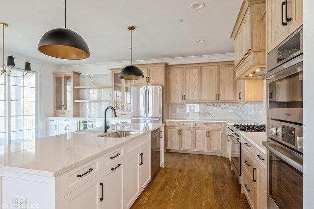 kitchen with appliances with stainless steel finishes, light brown cabinetry, open shelves, backsplash, and a kitchen island with sink