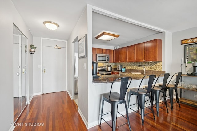 525 W Hawthorne Pl Unit 1004, Chicago, IL 60657 - kitchen featuring appliances with stainless steel finishes, wood finished floors, decorative backsplash, dark stone counters, and a breakfast bar area
