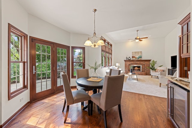 609 Spruce Ct, Oswego, IL 60543 - dining space featuring wine cooler, light wood-style floors, a fireplace, a chandelier, and ceiling fan
