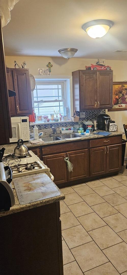 1601 44th Ave, Stone Park, IL 60165 - kitchen featuring white microwave, decorative backsplash, light tile patterned floors, and dark brown cabinetry