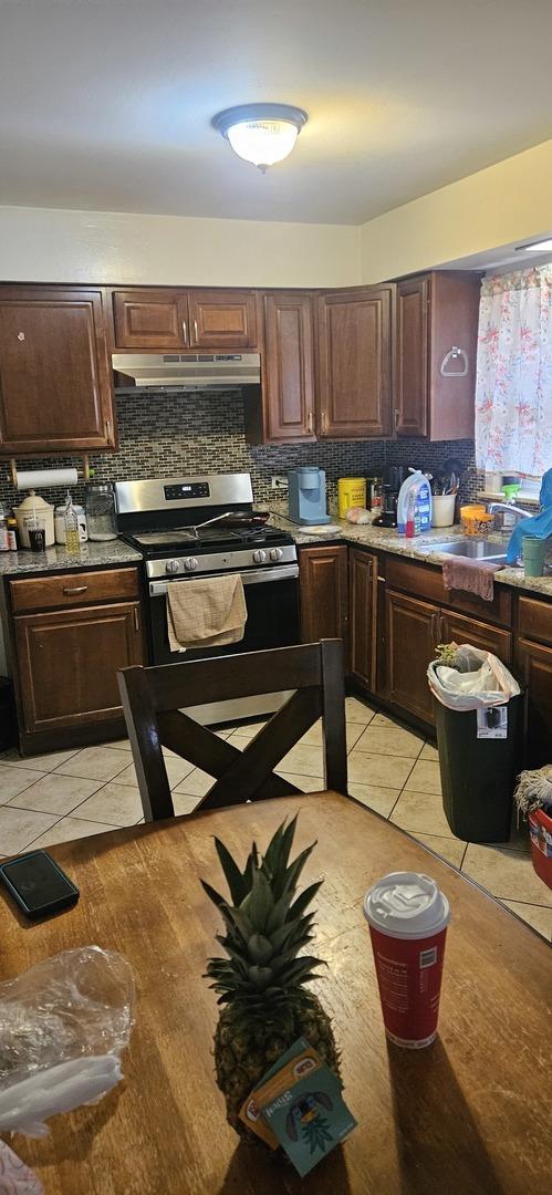 1601 44th Ave, Stone Park, IL 60165 - kitchen with gas range, under cabinet range hood, tasteful backsplash, and light tile patterned floors