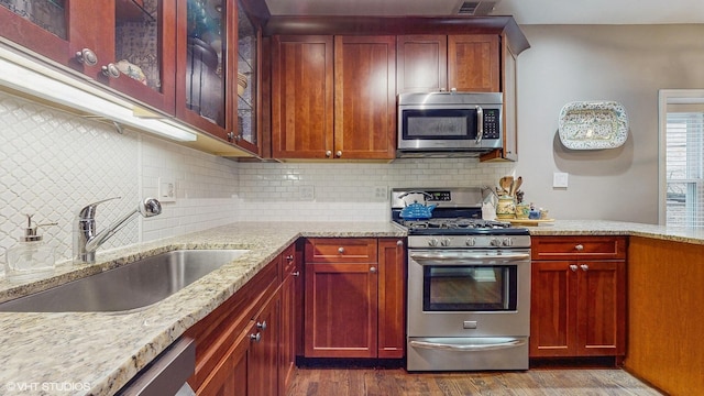 4550 N Malden St Unit 1W, Chicago, IL 60640 - kitchen featuring appliances with stainless steel finishes, light stone counters, dark wood-style floors, glass insert cabinets, and backsplash