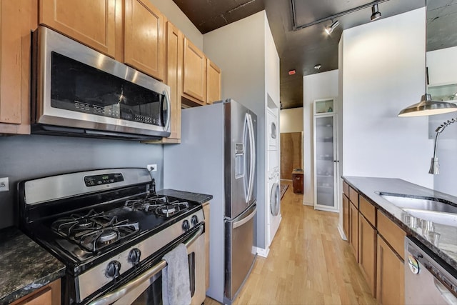 1122 W Catalpa Ave Unit 815, Chicago, IL 60640 - kitchen with appliances with stainless steel finishes, stacked washing machine and dryer, light wood finished floors, dark stone countertops, and brown cabinetry