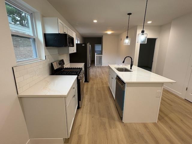 8317 S Constance Ave, Chicago, IL 60617 - kitchen featuring black microwave, stainless steel gas stove, dishwashing machine, light wood-type flooring, and white cabinets