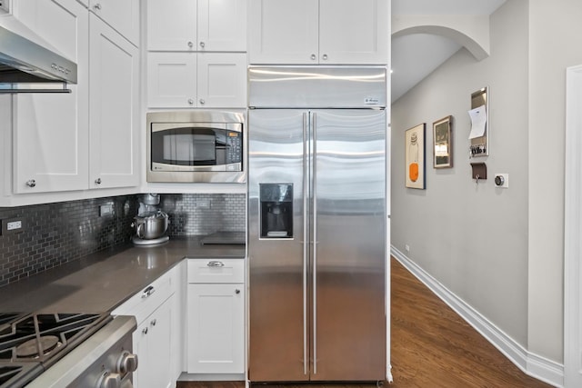 841 W Monroe St Unit 4A, Chicago, IL 60607 - kitchen featuring built in appliances, wall chimney range hood, decorative backsplash, white cabinets, and dark countertops