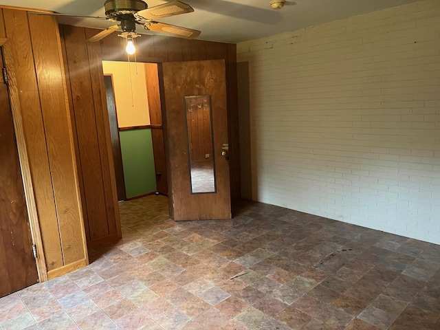 2075 Halsey Dr, Des Plaines, IL 60018 - empty room featuring stone finish flooring, brick wall, wood walls, and ceiling fan