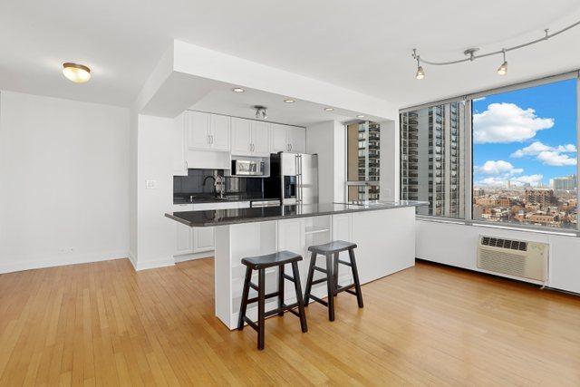 70 W Burton Pl Unit 1801, Chicago, IL 60610 - kitchen featuring appliances with stainless steel finishes, dark countertops, light wood finished floors, a kitchen breakfast bar, and white cabinets