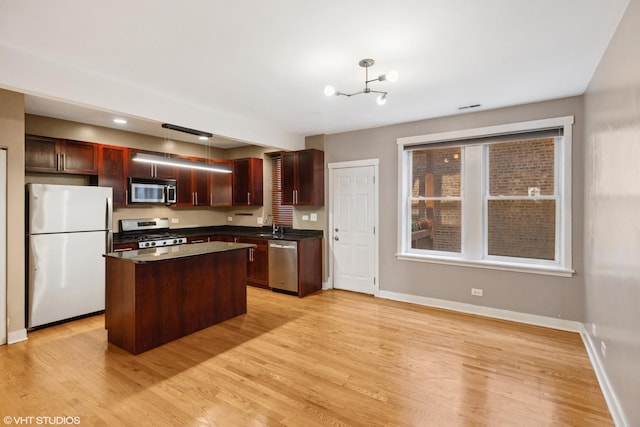 2305 N Kimball Ave Unit 1, Chicago, IL 60647 - kitchen featuring appliances with stainless steel finishes, dark countertops, light wood finished floors, a center island, and a chandelier