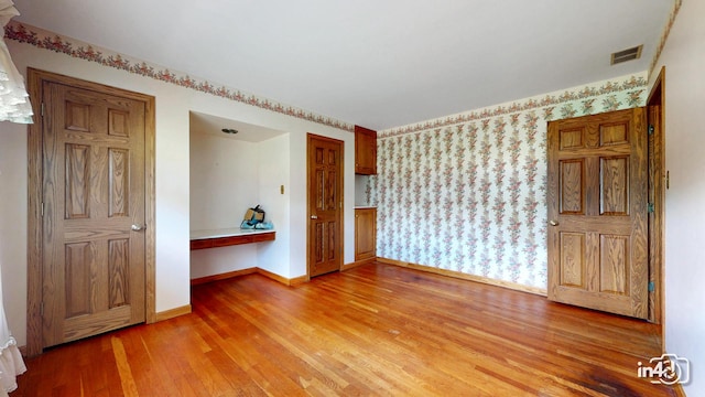 74 Wilmette Dr, Oswego, IL 60543 - empty room featuring light wood finished floors, built in desk, and wallpapered walls