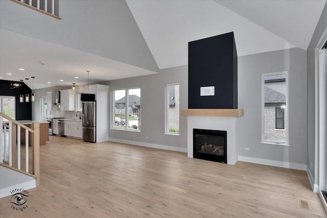 16451 Kayla Dr, Lemont, IL 60439 - unfurnished living room with light wood-type flooring, high vaulted ceiling, stairway, a glass covered fireplace, and healthy amount of natural light