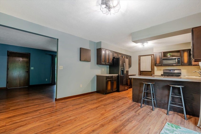 106 Sandra Ln, Normal, IL 61761 - kitchen featuring appliances with stainless steel finishes, dark brown cabinetry, light wood-type flooring, tasteful backsplash, and a peninsula