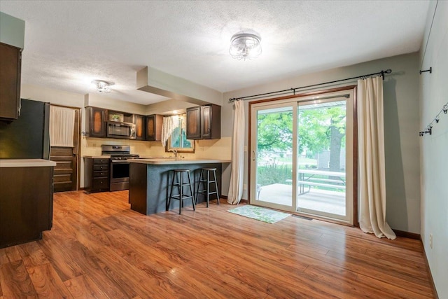 106 Sandra Ln, Normal, IL 61761 - kitchen with stainless steel appliances, a peninsula, a breakfast bar, light wood-style flooring, and a textured ceiling