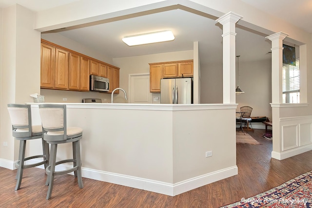 13399 Glenwood Dr, Huntley, IL 60142 - kitchen featuring appliances with stainless steel finishes, a peninsula, ornate columns, wood finished floors, and a kitchen breakfast bar