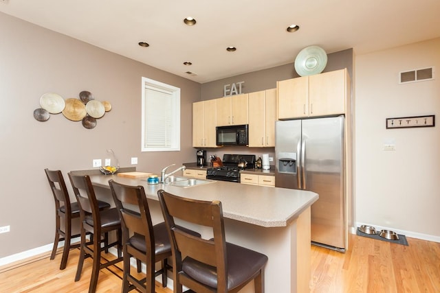 4124 N Kenmore Ave Unit Gs, Chicago, IL 60613 - kitchen featuring black appliances, a peninsula, light wood-style flooring, a kitchen breakfast bar, and light brown cabinetry