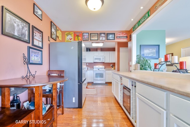 kitchen with white appliances, white cabinets, light wood-type flooring, and light countertops