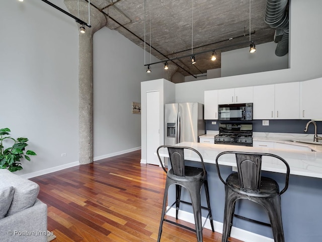 900 N Kingsbury St Unit 967, Chicago, IL 60610 - kitchen with black appliances, rail lighting, a towering ceiling, a kitchen breakfast bar, and white cabinetry