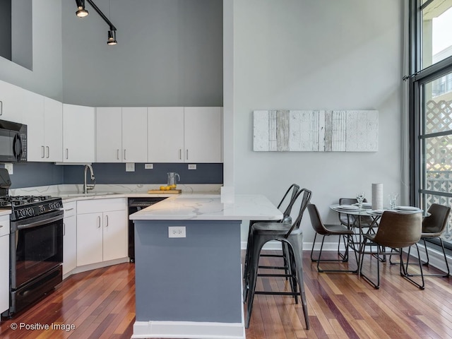 900 N Kingsbury St Unit 967, Chicago, IL 60610 - kitchen featuring black appliances, a towering ceiling, hardwood / wood-style flooring, a peninsula, and light stone countertops