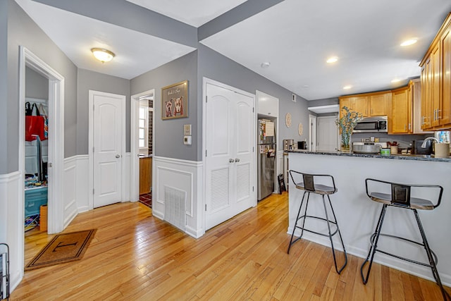 4825 N Karlov Ave, Chicago, IL 60630 - kitchen with appliances with stainless steel finishes, a peninsula, light wood finished floors, wainscoting, and a breakfast bar