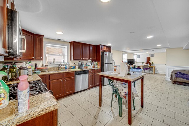 4825 N Karlov Ave, Chicago, IL 60630 - kitchen with stainless steel appliances, open floor plan, wainscoting, reddish brown cabinets, and light stone countertops