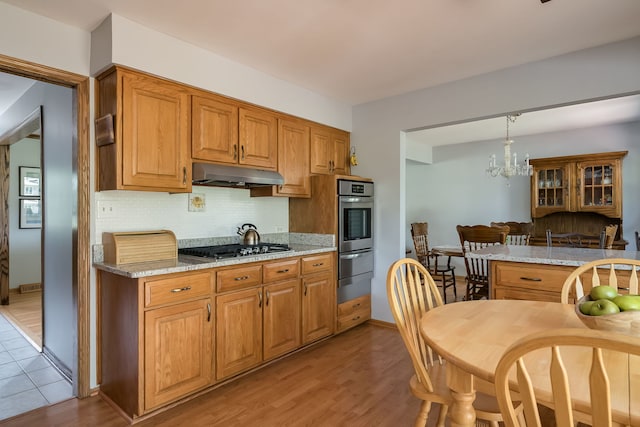 9S339 Cumnor Rd, Downers Grove, IL 60516 - kitchen featuring appliances with stainless steel finishes, under cabinet range hood, backsplash, light wood-style floors, and a chandelier