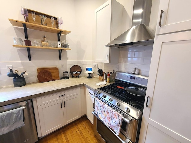 313 S 4th St, Oregon, IL 61061 - kitchen featuring wall chimney range hood, stainless steel appliances, white cabinets, light countertops, and wood-type flooring