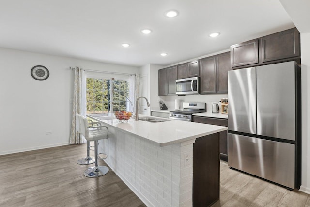 1917 Turtle Creek Ct, Aurora, IL 60503 - kitchen featuring appliances with stainless steel finishes, dark brown cabinets, a kitchen island with sink, a breakfast bar area, and light wood-style flooring