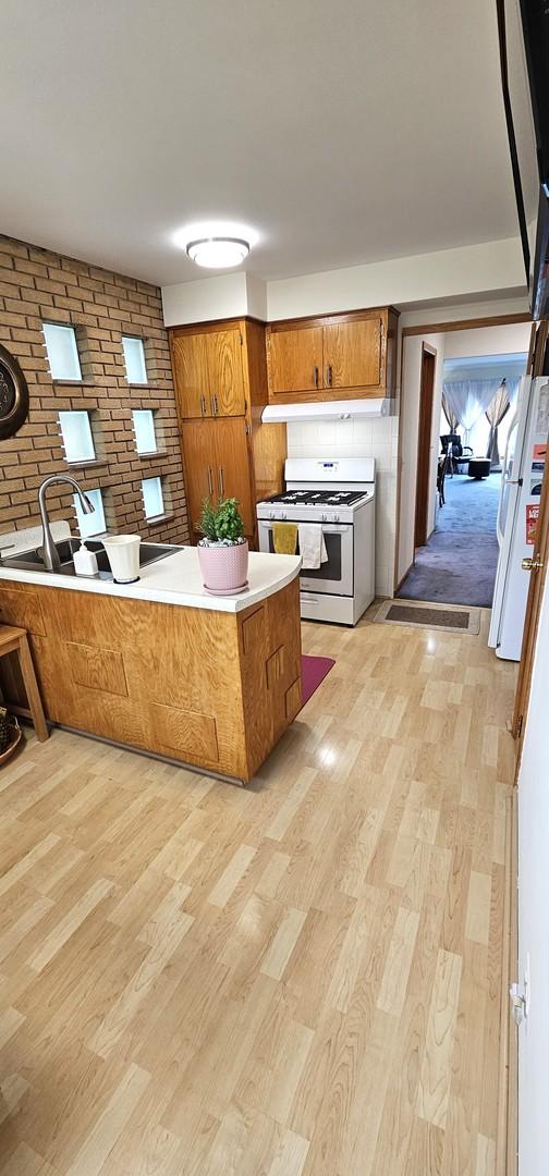 5705 N Oketo Ave, Chicago, IL 60631 - kitchen with white appliances, brown cabinets, light wood finished floors, brick wall, and light countertops
