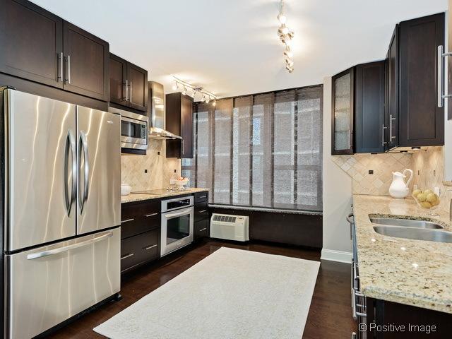 1550 N Lake Shore Dr Unit 3G, Chicago, IL 60610 - kitchen with stainless steel appliances, wall chimney exhaust hood, dark brown cabinetry, and decorative backsplash