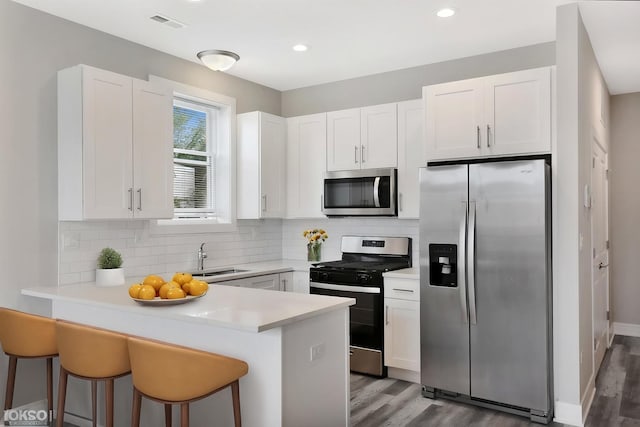 6349 S Maryland Ave, Chicago, IL 60637 - kitchen featuring stainless steel appliances, a peninsula, white cabinets, wood finished floors, and a breakfast bar area