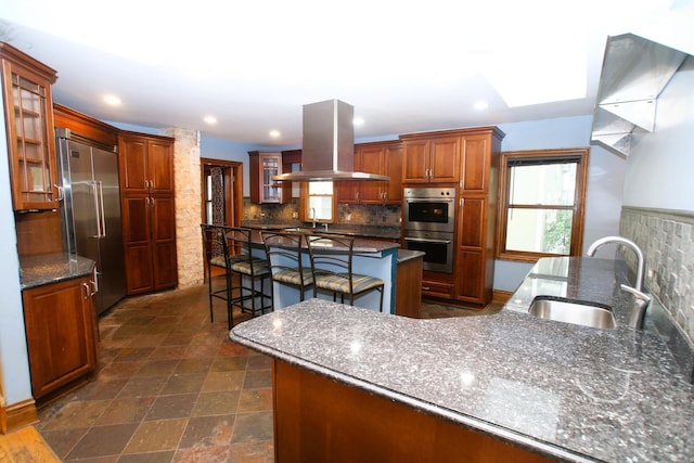 314 N Maple St, Itasca, IL 60143 - kitchen featuring stainless steel appliances, island exhaust hood, a breakfast bar, tasteful backsplash, and glass insert cabinets