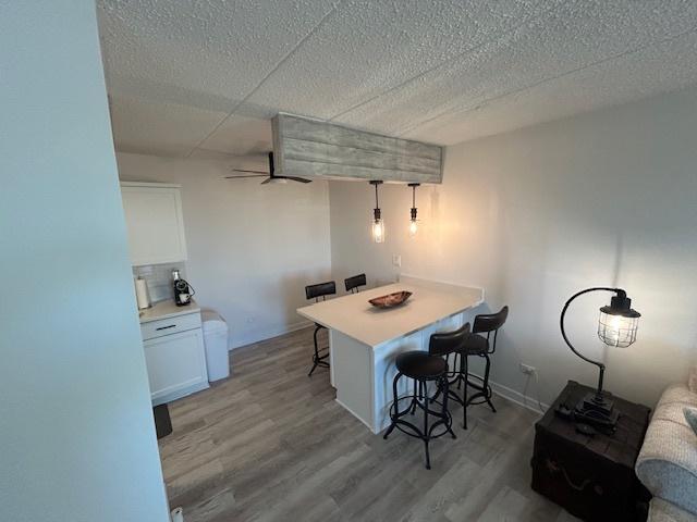 9098 Terrace Dr Unit 3E, Niles, IL 60714 - kitchen featuring a breakfast bar, a ceiling fan, light wood-style floors, white cabinetry, and a textured ceiling