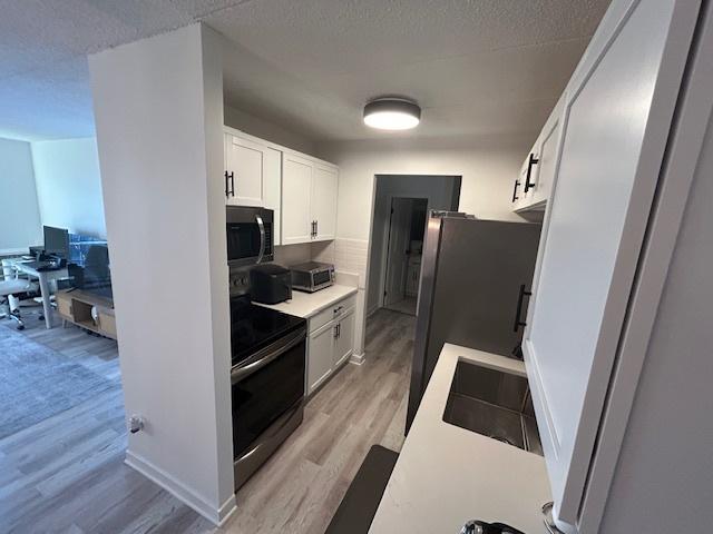 9098 Terrace Dr Unit 3E, Niles, IL 60714 - kitchen with appliances with stainless steel finishes, light wood-style flooring, white cabinetry, a desk, and light countertops
