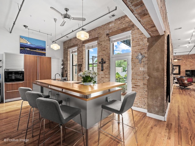 2035 W Charleston St Unit 205, Chicago, IL 60647 - kitchen with butcher block counters, brick wall, light wood-style floors, a ceiling fan, and a kitchen bar