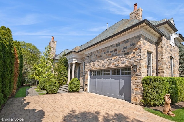 78 Wagner Rd, Northfield, IL 60093 - view of home's exterior featuring an attached garage, stone siding, a chimney, and driveway