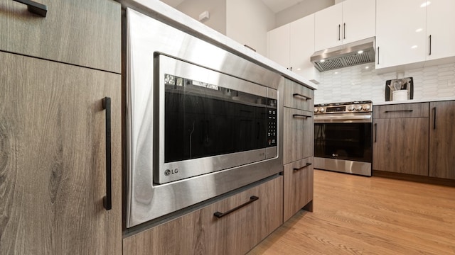 3124 S Benson St Unit 6, Chicago, IL 60608 - kitchen with stainless steel appliances, under cabinet range hood, tasteful backsplash, light wood-style flooring, and white cabinetry