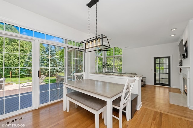dining area with light wood-style floors, a chandelier, plenty of natural light, a fireplace with flush hearth, and recessed lighting
